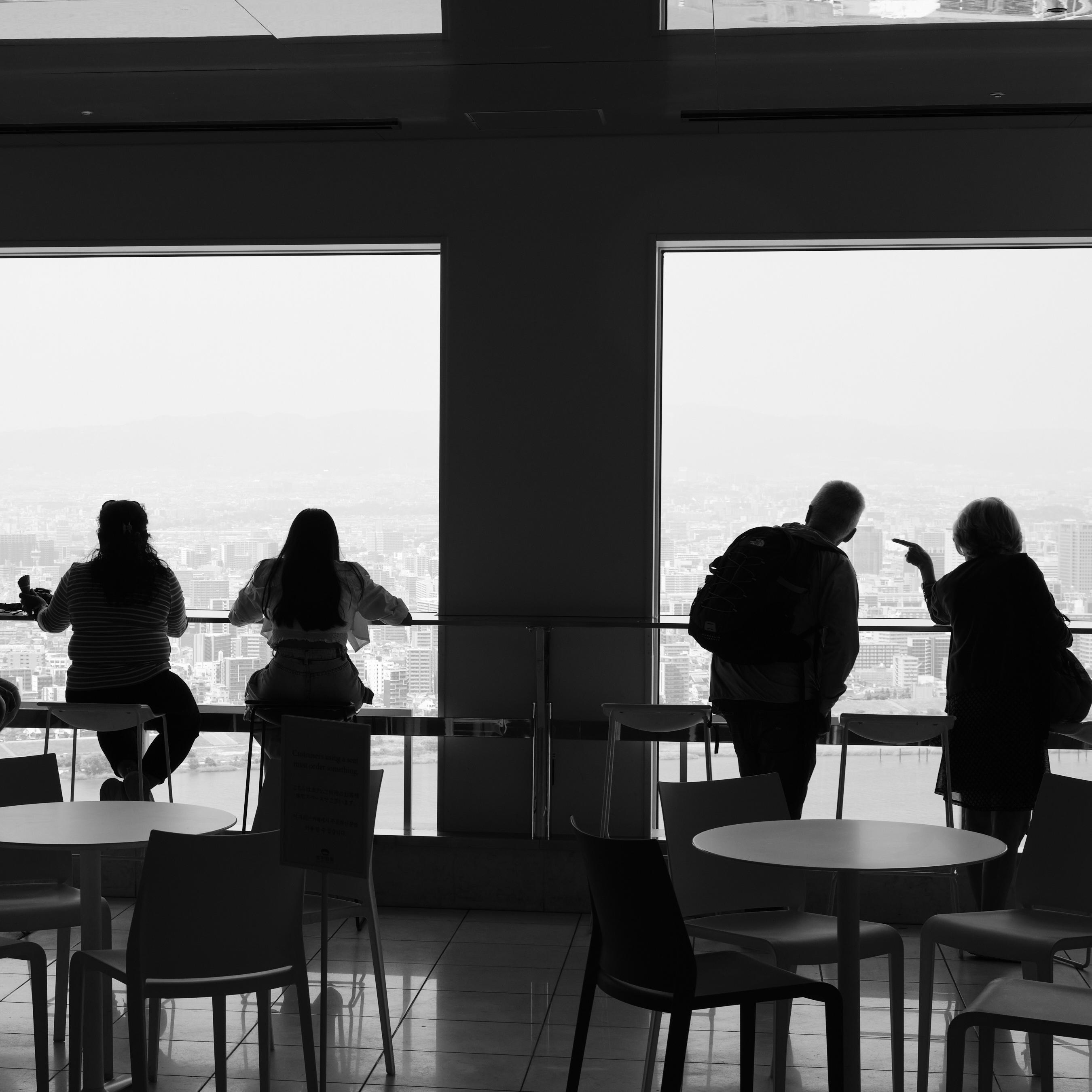 Black and white photo of people inside Umeda Sky Building in Osaka. They look out of the windows.